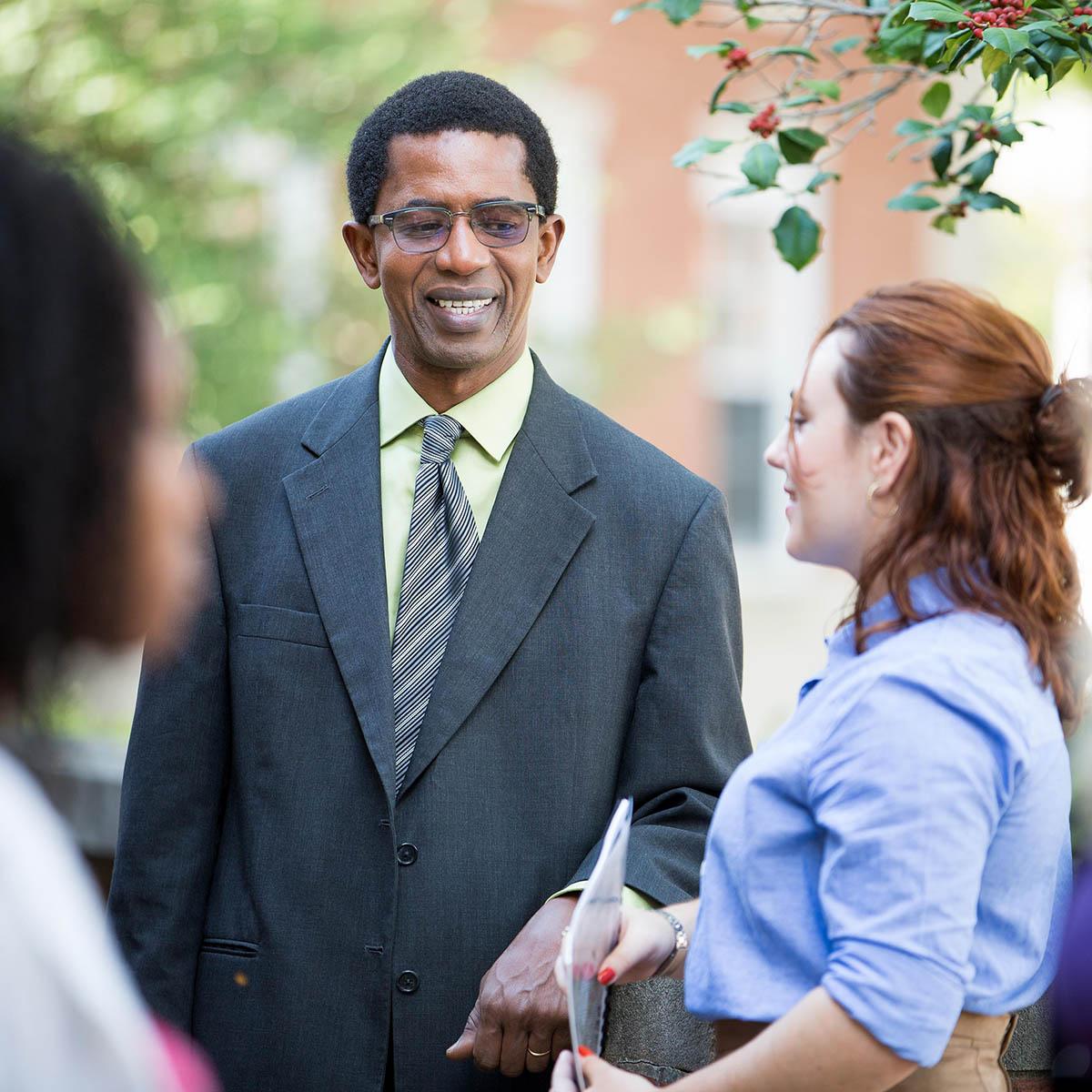 Photo of Jean Jacques Sene smiling and speaking with students at an outdoor reception